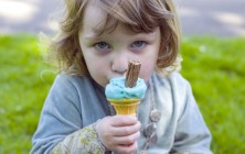 Young girl eating a blue ice cream in a park