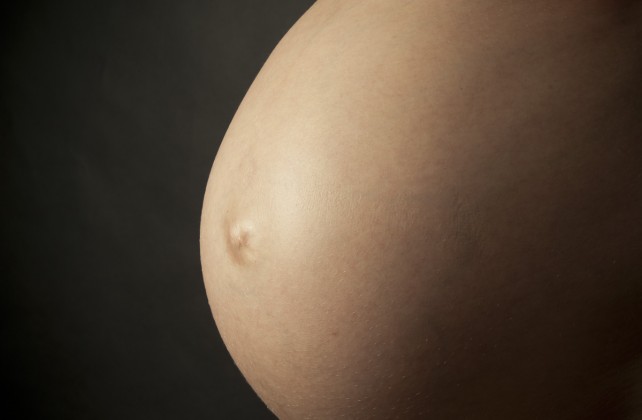 Close up of pregnant belly on black background