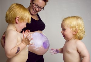 Two young boys painting their mother's bump